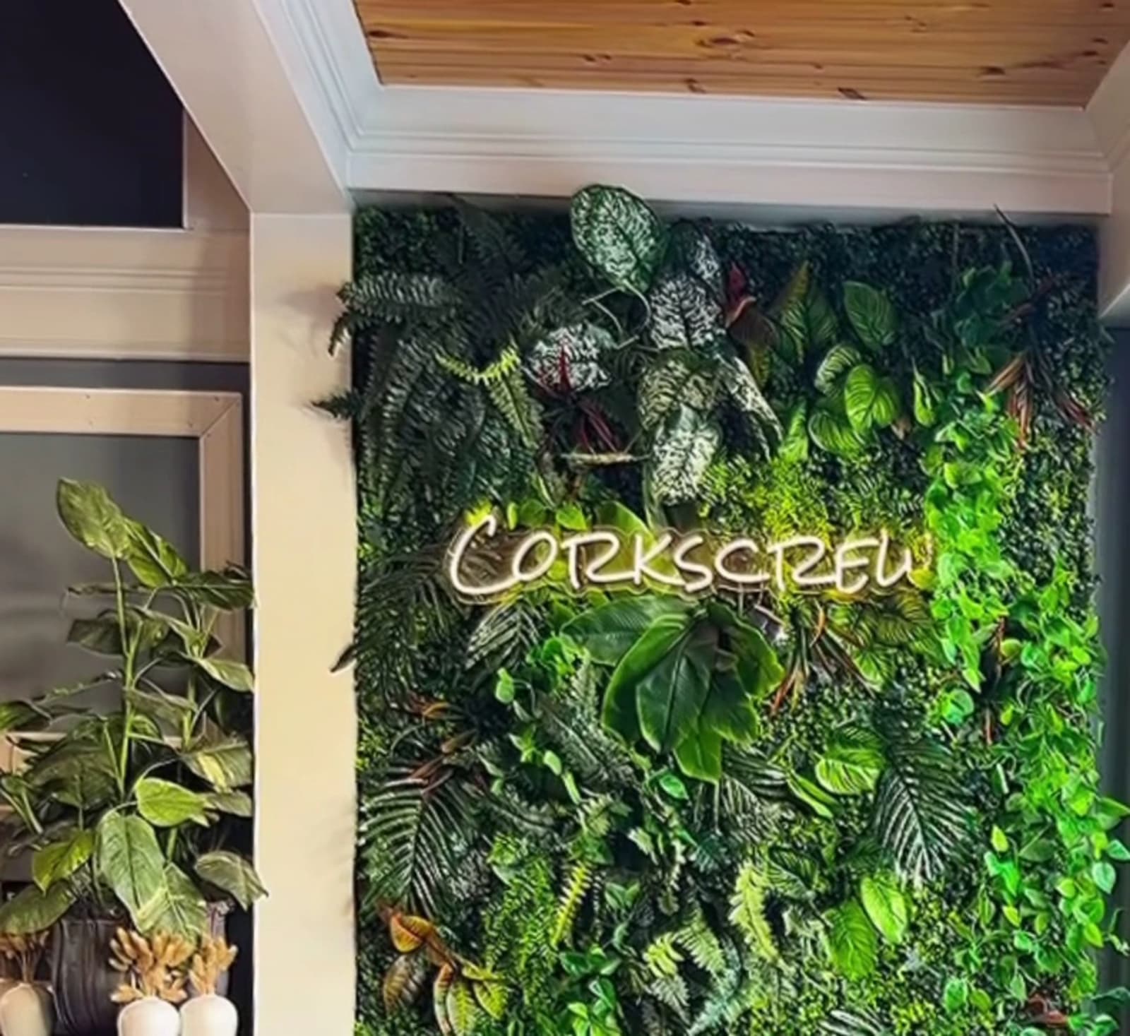 The Corkscrew name in neon script on a wall of living plants