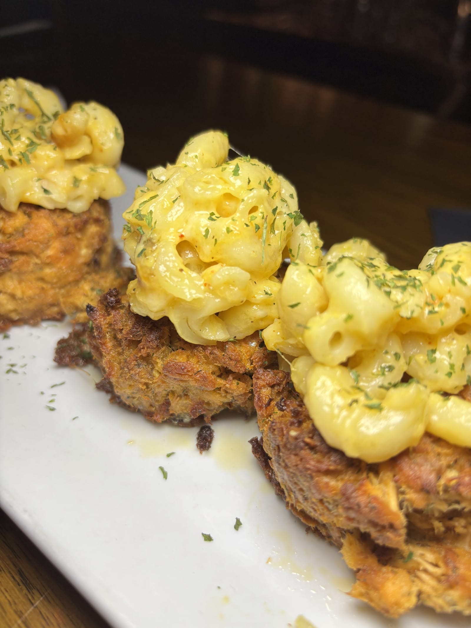 Crab cakes topped with mac and cheese on a white plate