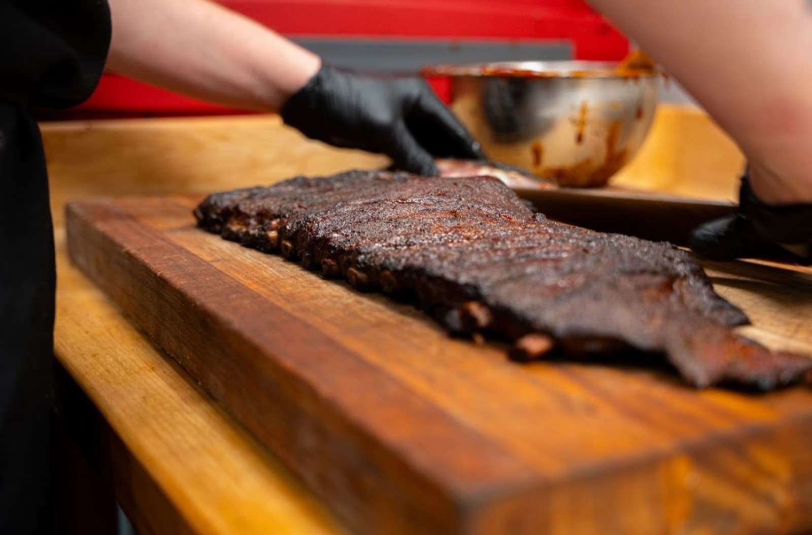 Gloved hands mopping sauce onto a rack of smoked ribs