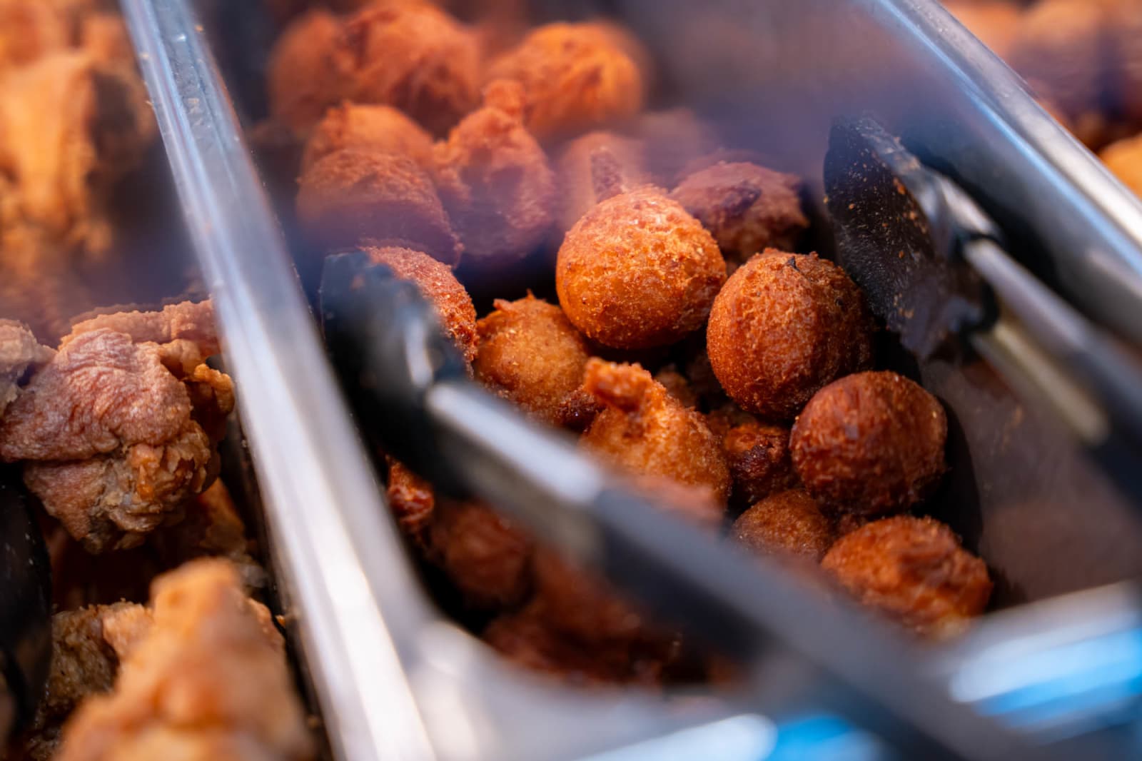 Hushpuppies and fried chicken in a serving pan with tongs