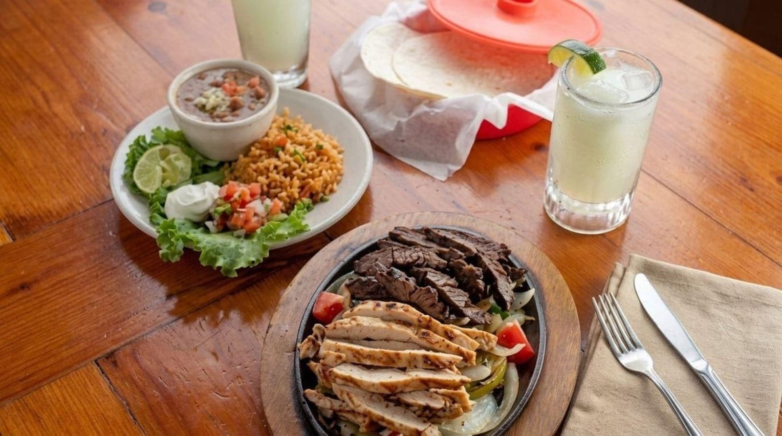A table set with sizzling fajitas, rice, pico, warm tortillas and a margarita