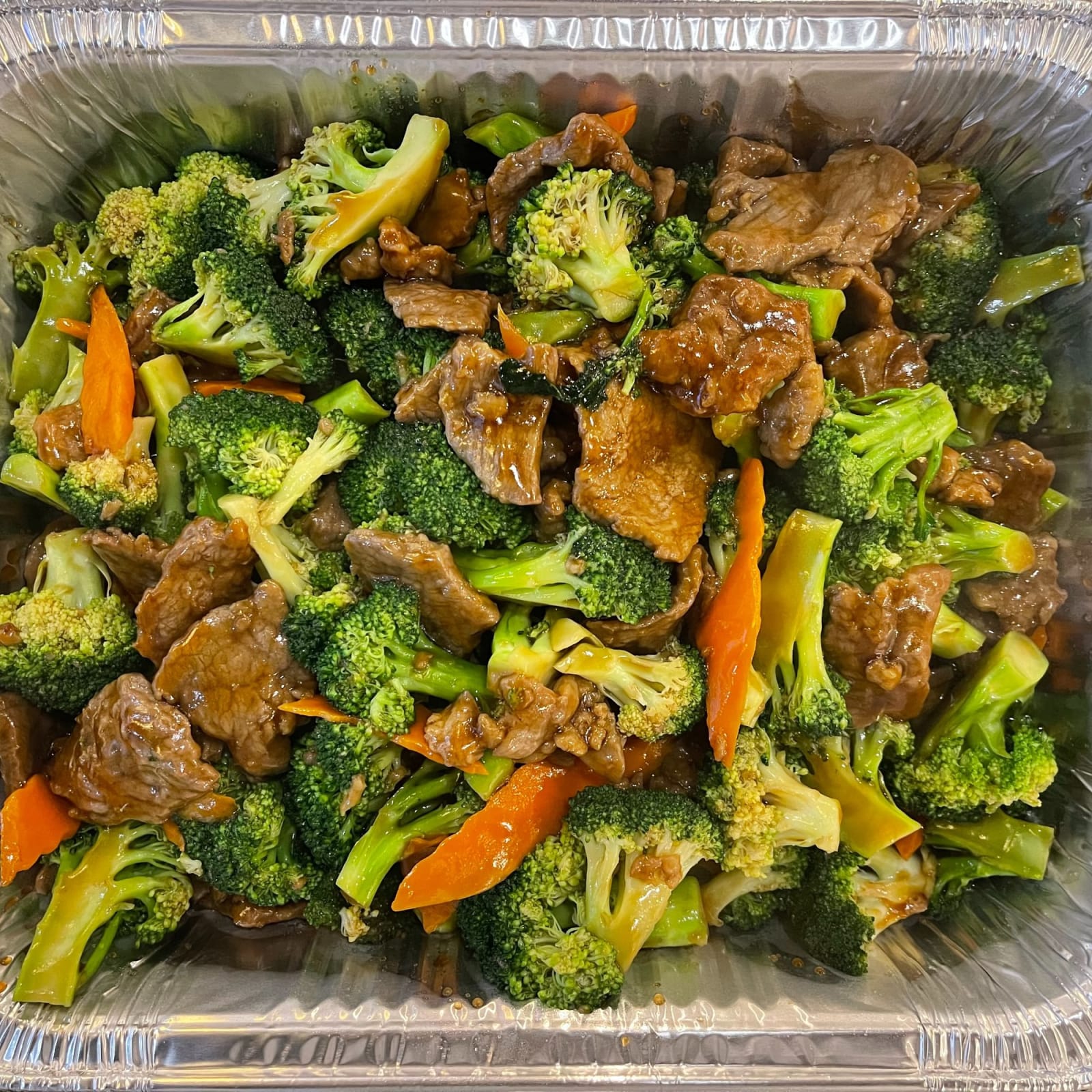 A foil catering pan of beef and broccoli with carrot, seen from above