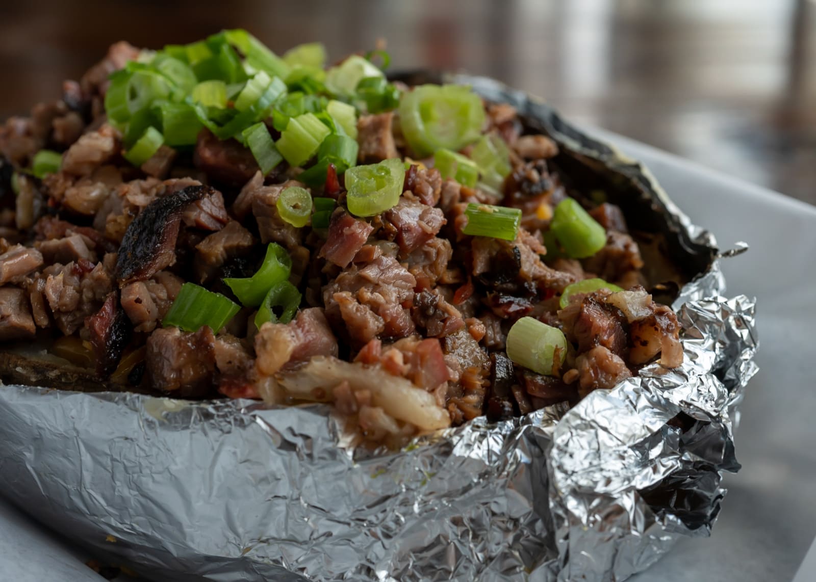 A stuffed baked potato topped with chopped brisket and green onion