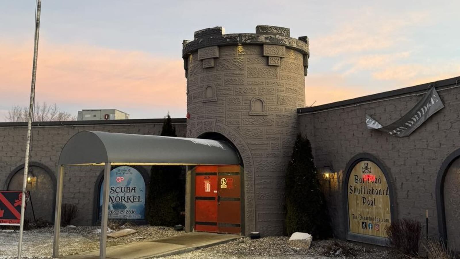 The castle tower and arched window signage at The Drawbridge at sunset