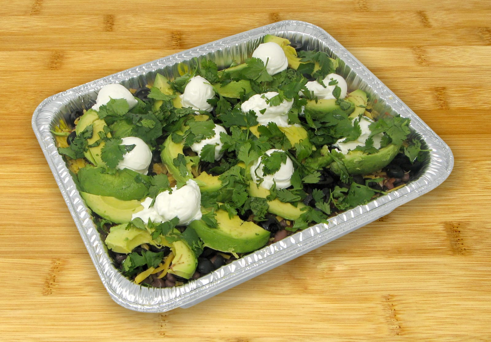 A Hyperbowle catering tray of rice and beans topped with avocado, sour cream and cilantro