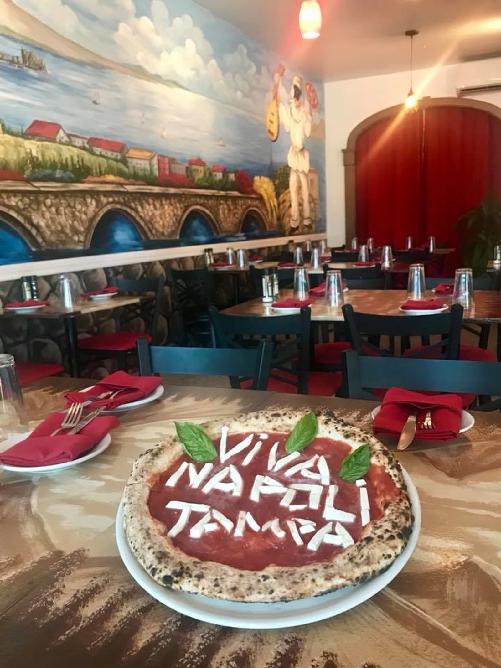 A pizza iced with VIVA NAPOLI TAMPA on a table in the mural dining room