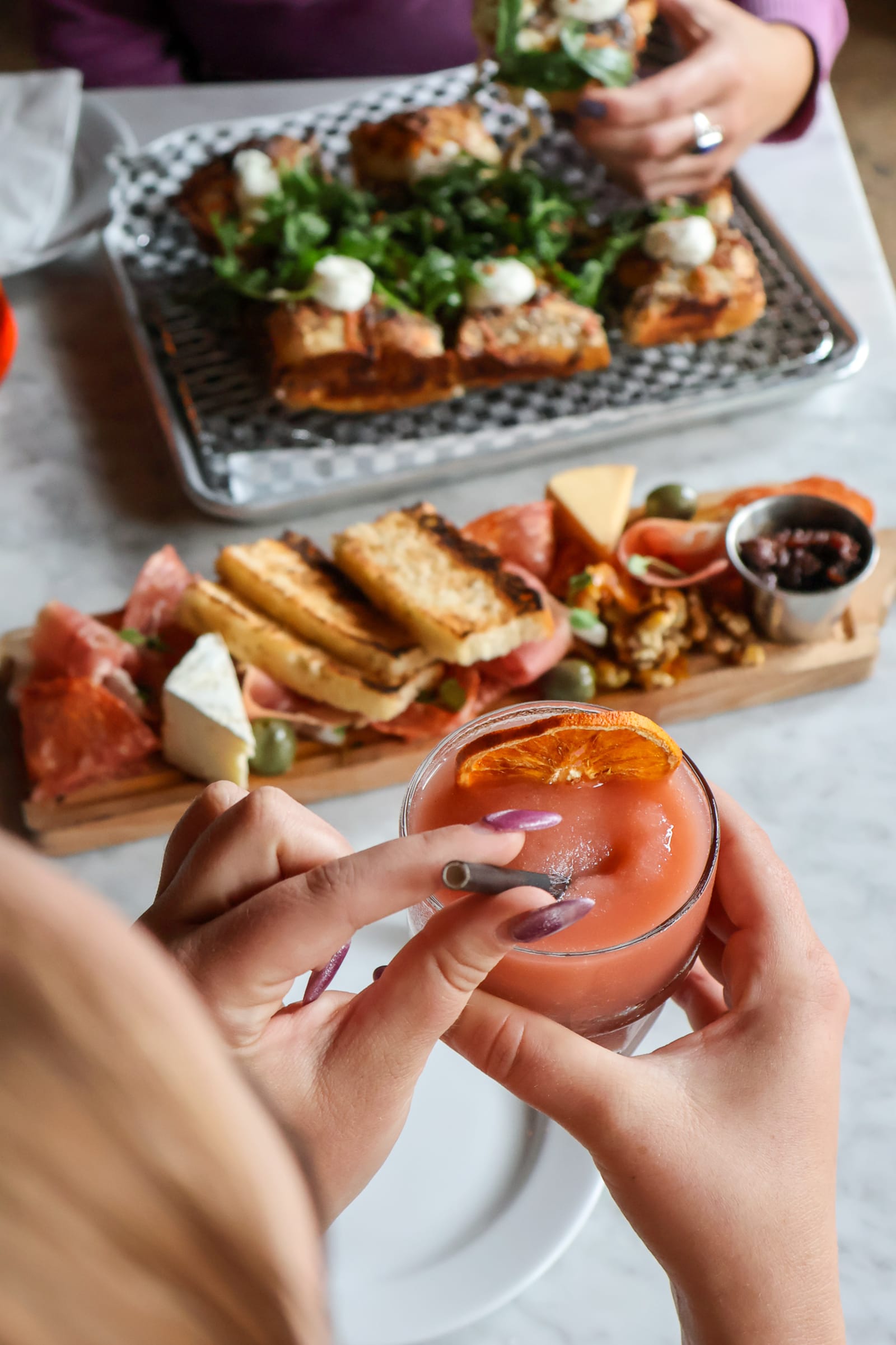 A shared board of cured meats and cheese beside a cocktail at the bar