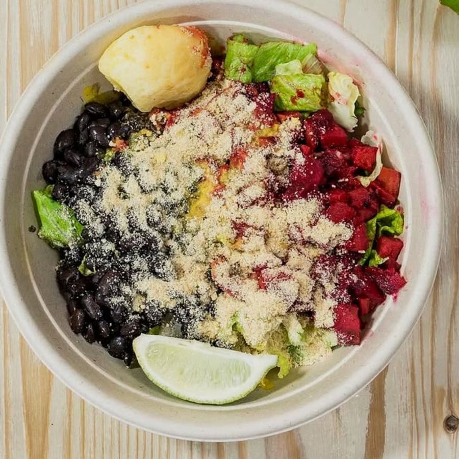 Brazilian bowl with black beans, greens and a lime wedge on a weathered wood table