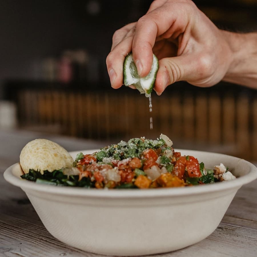 A hand squeezing fresh lime over a Brazilian bowl with Pão de Queijo
