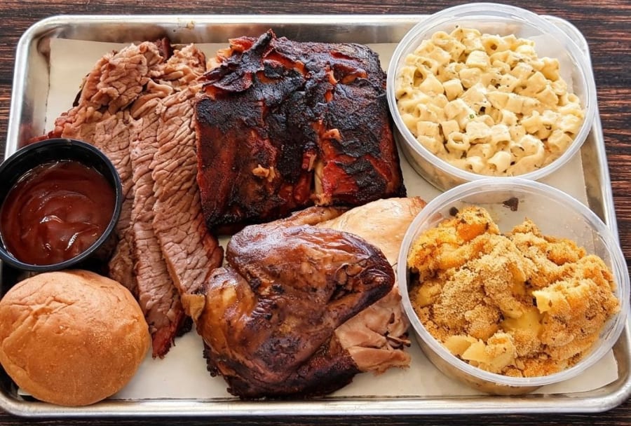 Tray of sliced smoked brisket, ribs, smoked chicken, mac and cheese and a dinner roll