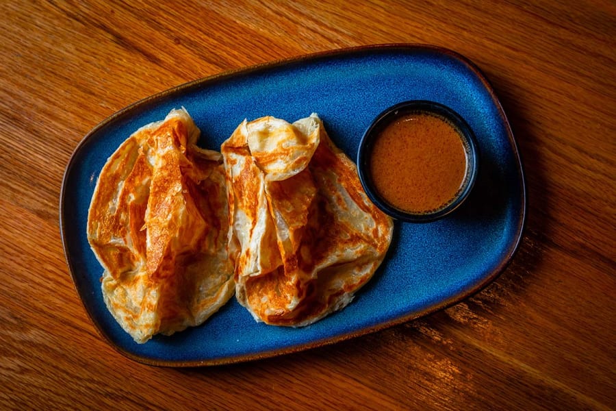 Roti canai torn open beside a bowl of curry dipping sauce