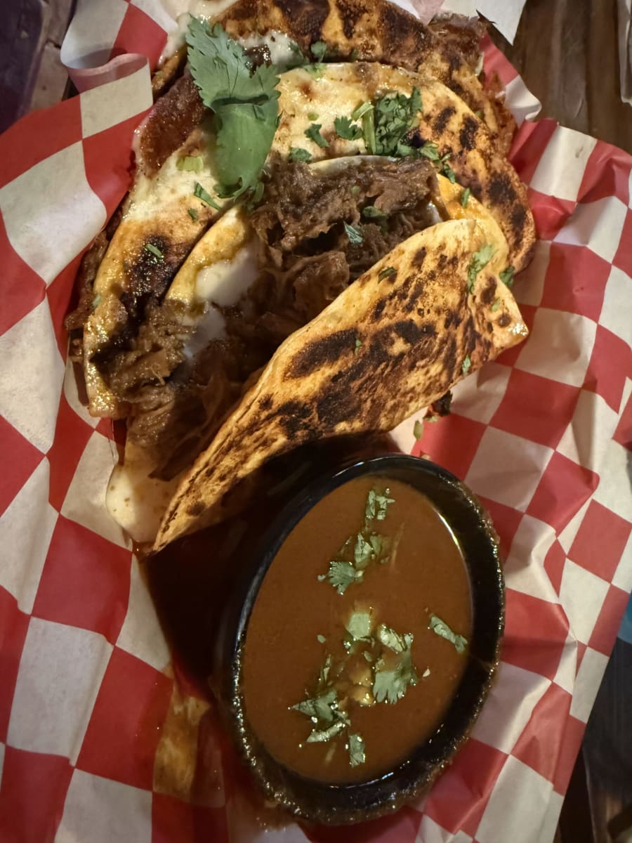 Birria tacos with consomme in a red-check basket