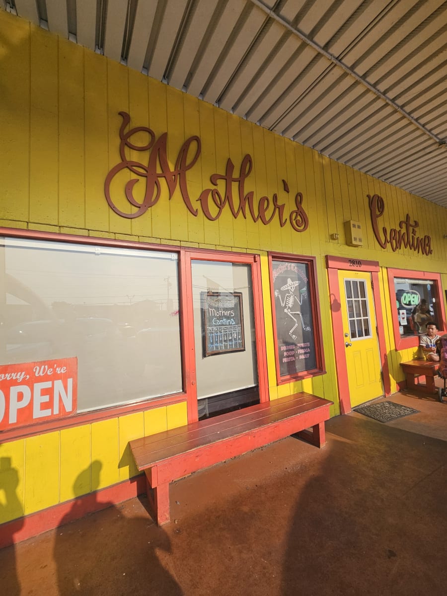 Mother's Cantina painted on the yellow exterior wall beside a red bench