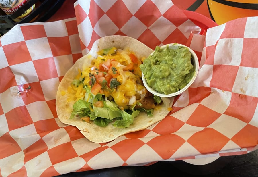 A single taco with guacamole in a red-check basket