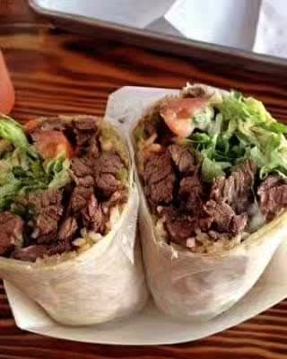 Two grilled steak burritos on a wood board