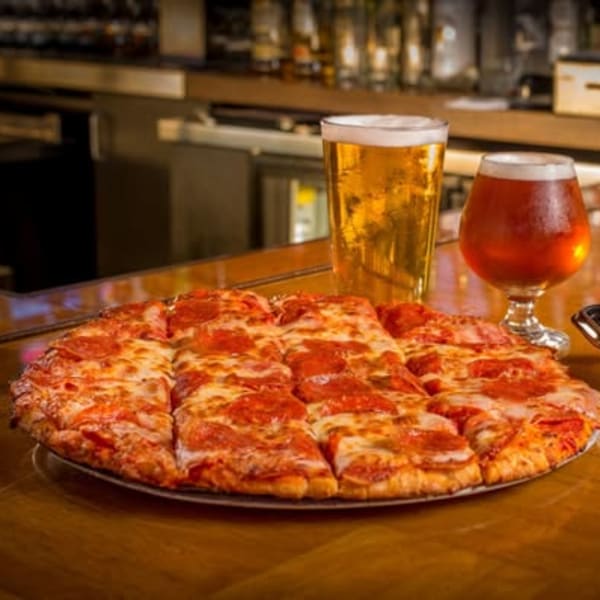 Pepperoni pizza with a basket of wings and two beers on the bar