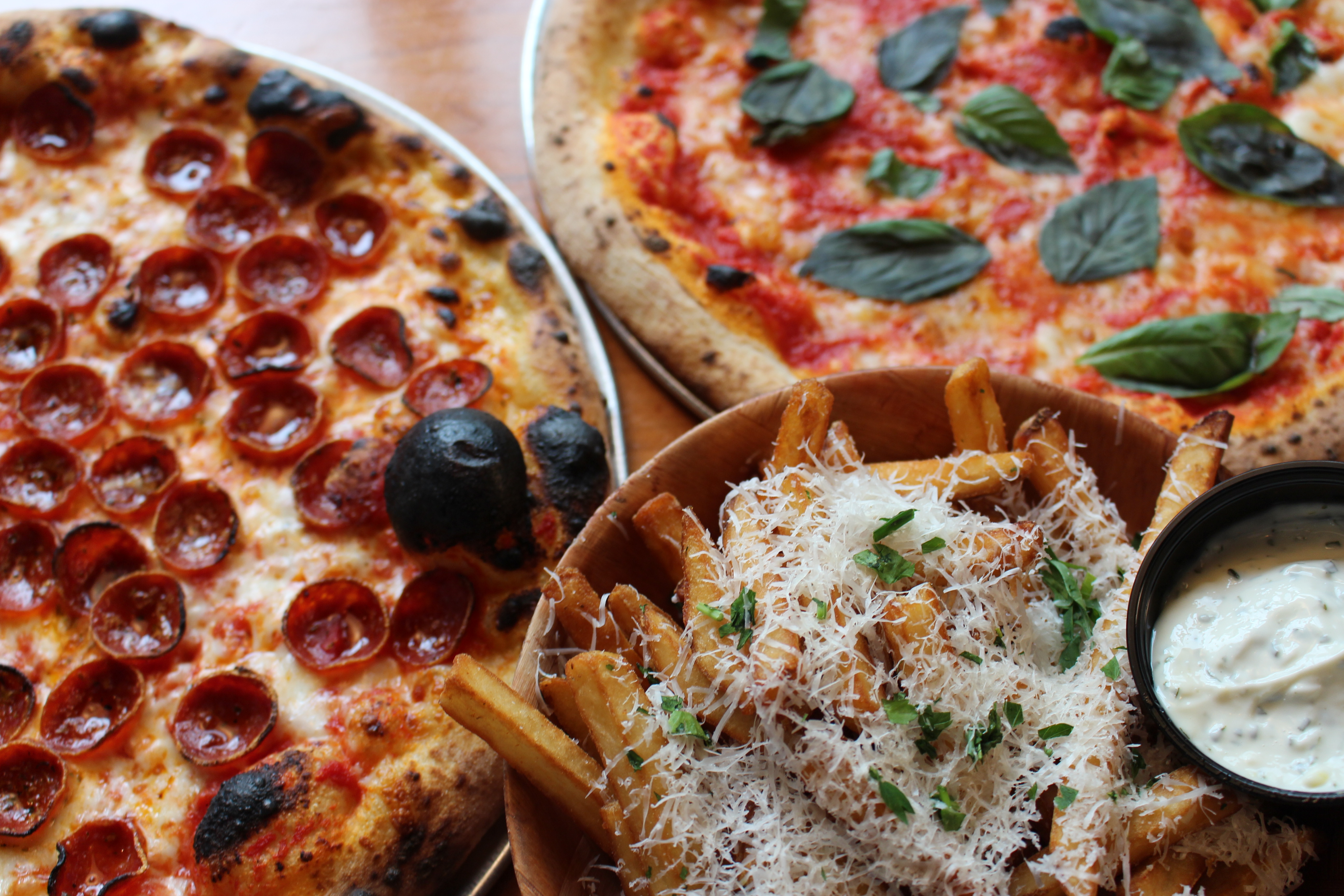 Two King Dough pizzas on trays — one with arugula, one red — on a wood table