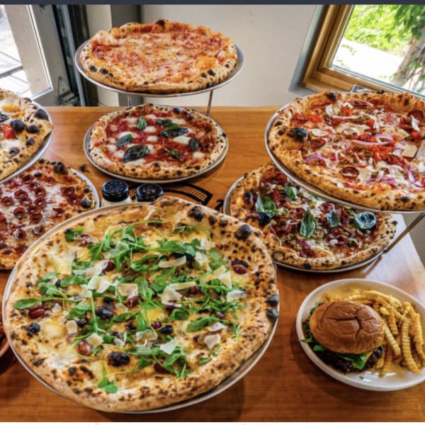 A spread of pizzas on stands with a burger and curly fries