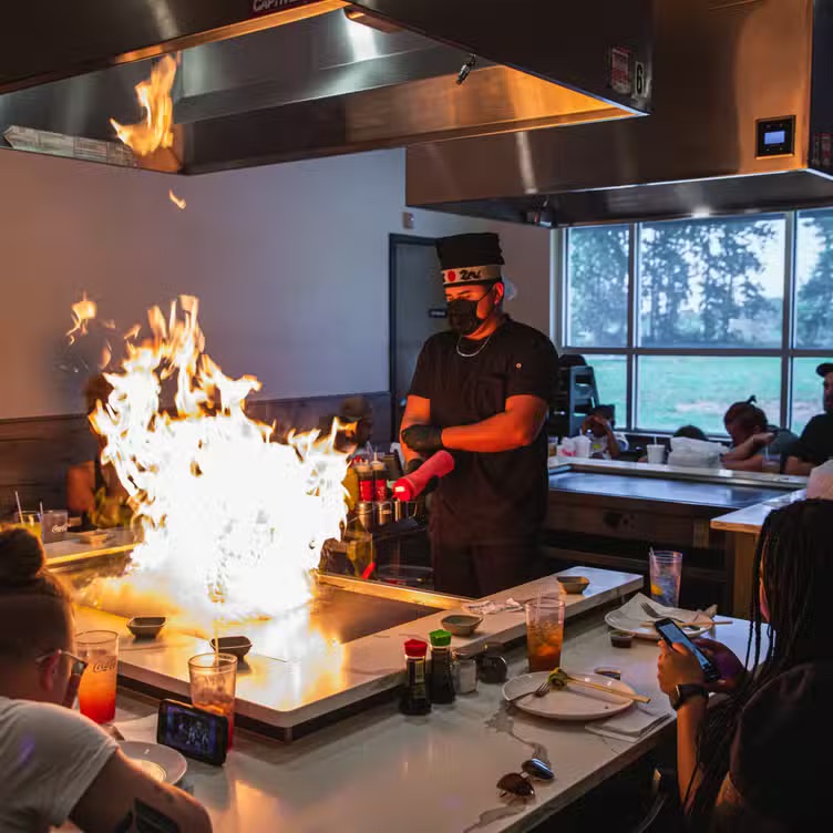 A hibachi chef cooking for a full table of guests at New Tokyo Hibachi