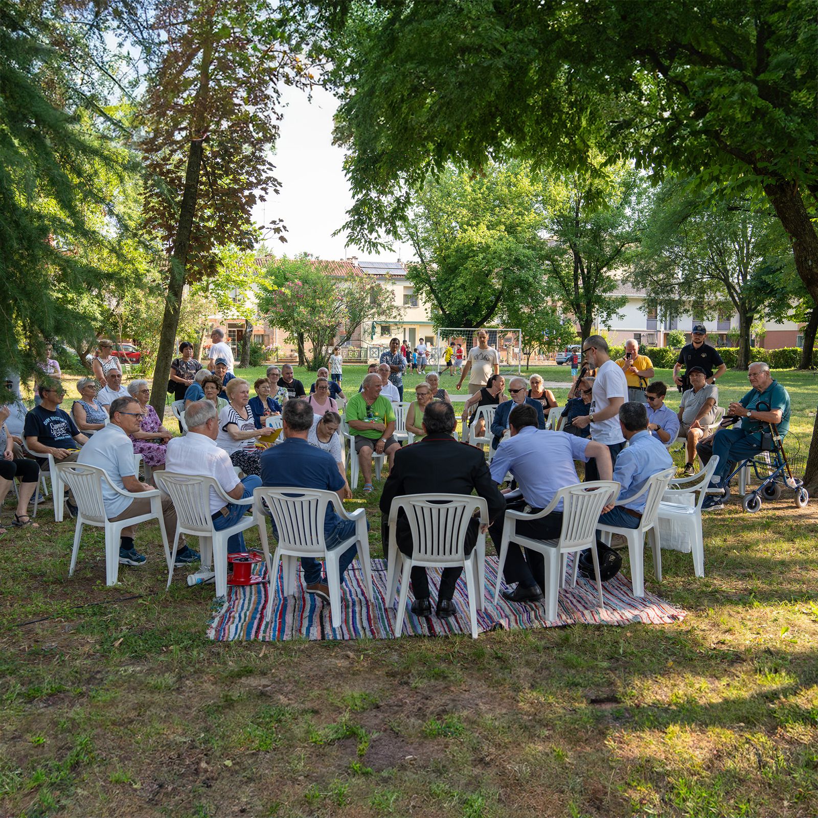 Assemblea di quartiere nel parco, sedie in cerchio sotto gli alberi