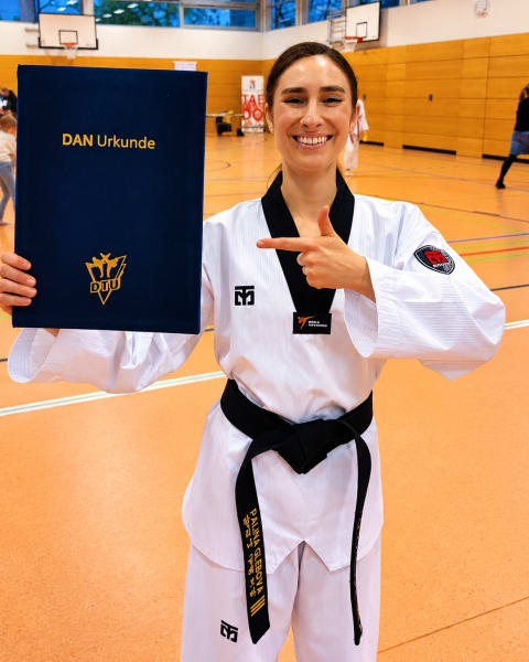 Palina Glebova im Dobok mit schwarzem Gürtel und Dan-Urkunde in der Sporthalle
