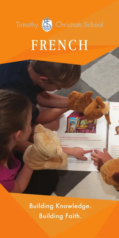 French Banner:  Two students are reading a French book together using puppets.