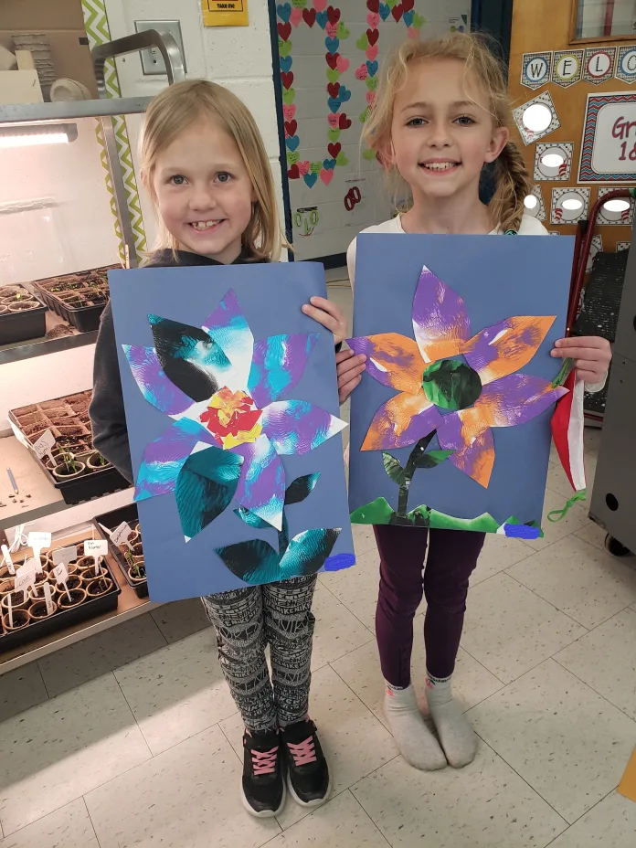 Two students are holding their flowery art work.