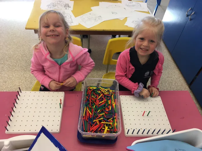 Two Kindergarten students are working with the coloured peg boards together.