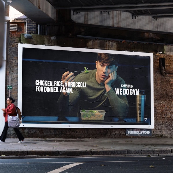 A billboard with a man eating, text "CHICKEN, RICE, & BROCCOLI FOR DINNER. AGAIN." and a passerby in motion blur.
