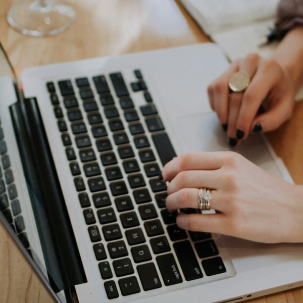 Person's hands on a laptop keyboard, wearing rings and a smartwatch.