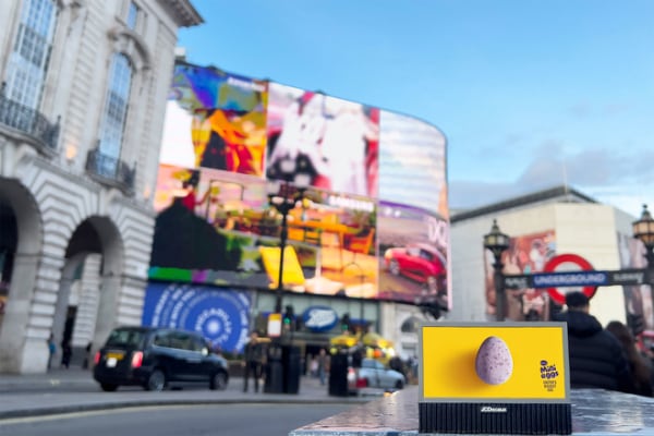 Piccadilly Circus with large screens, a blurred taxi, and a chocolate egg on a ledge in the foreground.