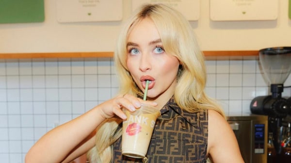 Blonde woman sipping a drink through a straw, with a playful expression, in a café setting.