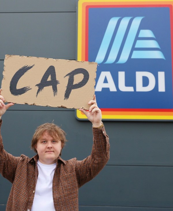 A person holds a sign reading "CAP" in front of an ALDI store.