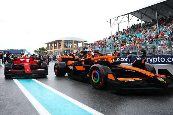 Two Formula 1 cars lined up on a wet track, with a crowd in the background.