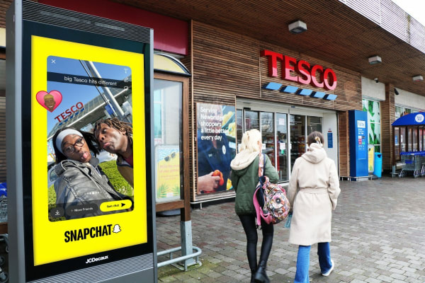 Two people pose humorously in front of a Tesco store; a Snapchat ad is displayed nearby.