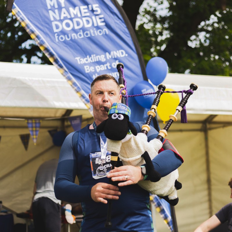 A man playing bagpipes wearing My Name'5 Doddie merchandise