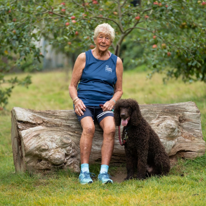 A smiling elderly woman in running gear sitting with her dog