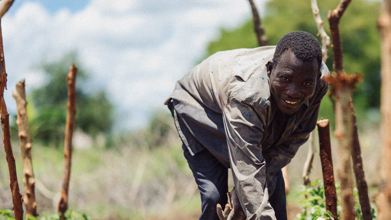 Smiling man bends to work the ground in a sunny outdoor field.