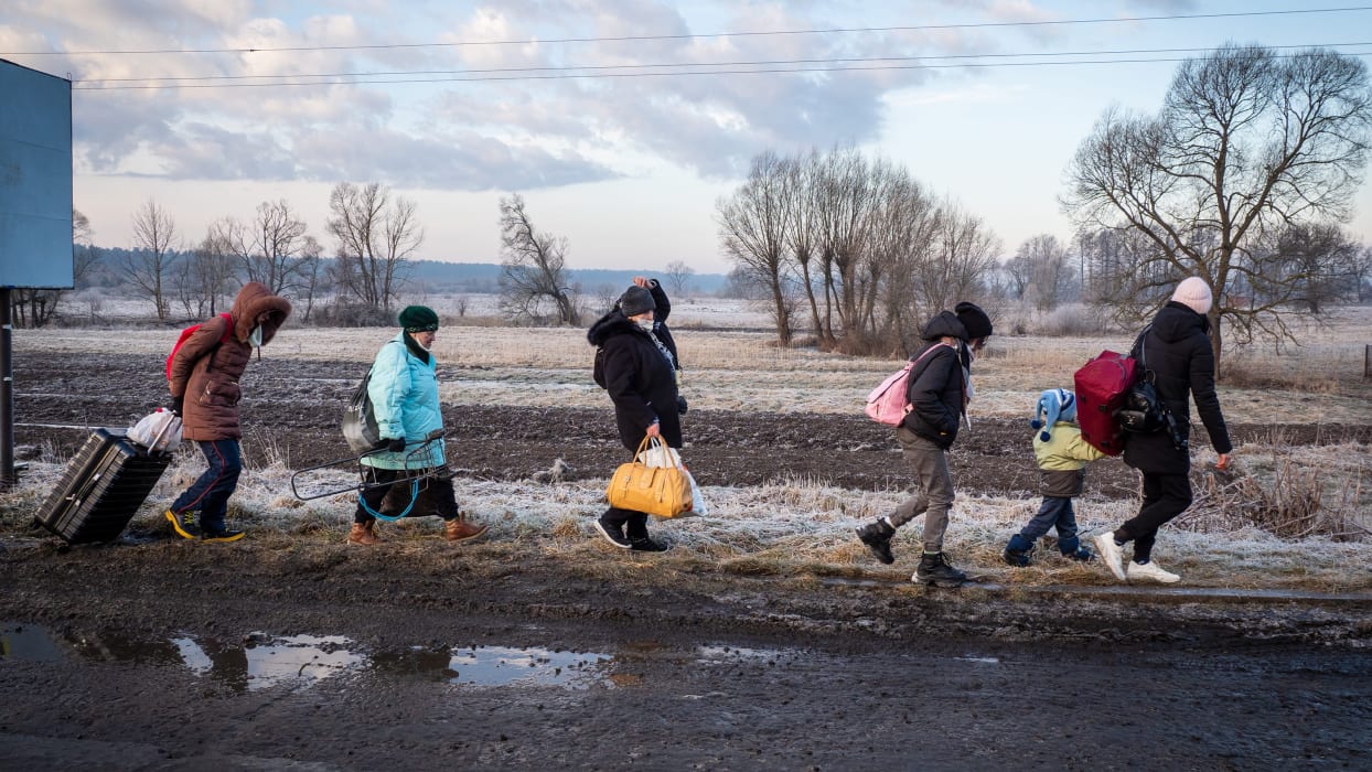 A group of people walk along a road carrying bags.
