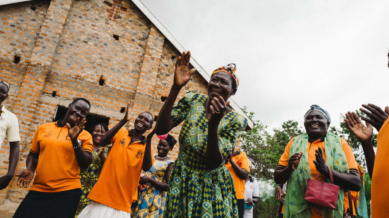 Joyful group of African women smiling and clapping outside a brick building.