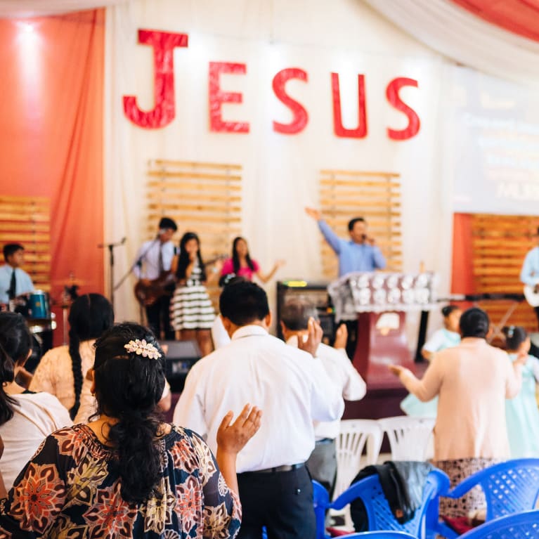 People worshiping in a church with the word Jesus in big letters on the wall