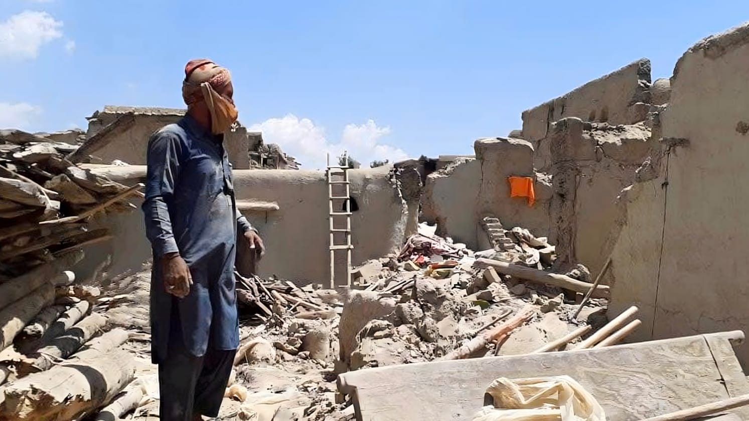 A person standing in front of a collapsed building amid rubble on the ground.