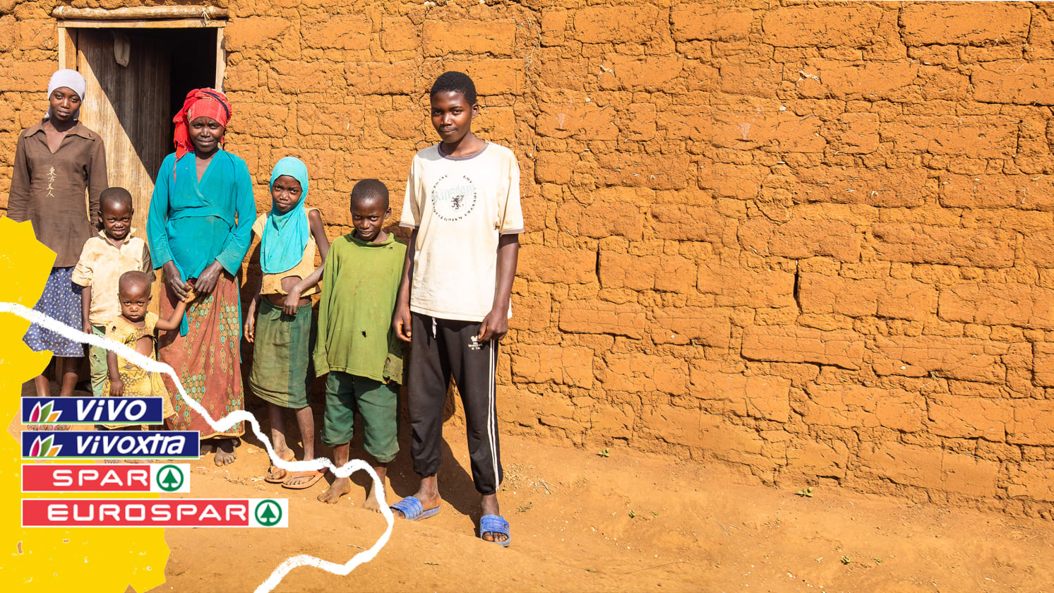 Two adults and five children of varying ages stand outside a building