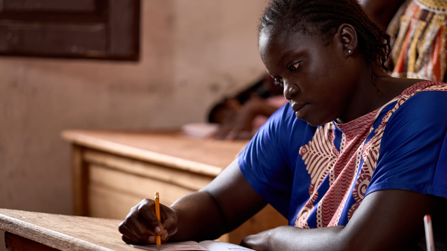 Davilla sits at a desk in a classroom writing with a pencil and paper.