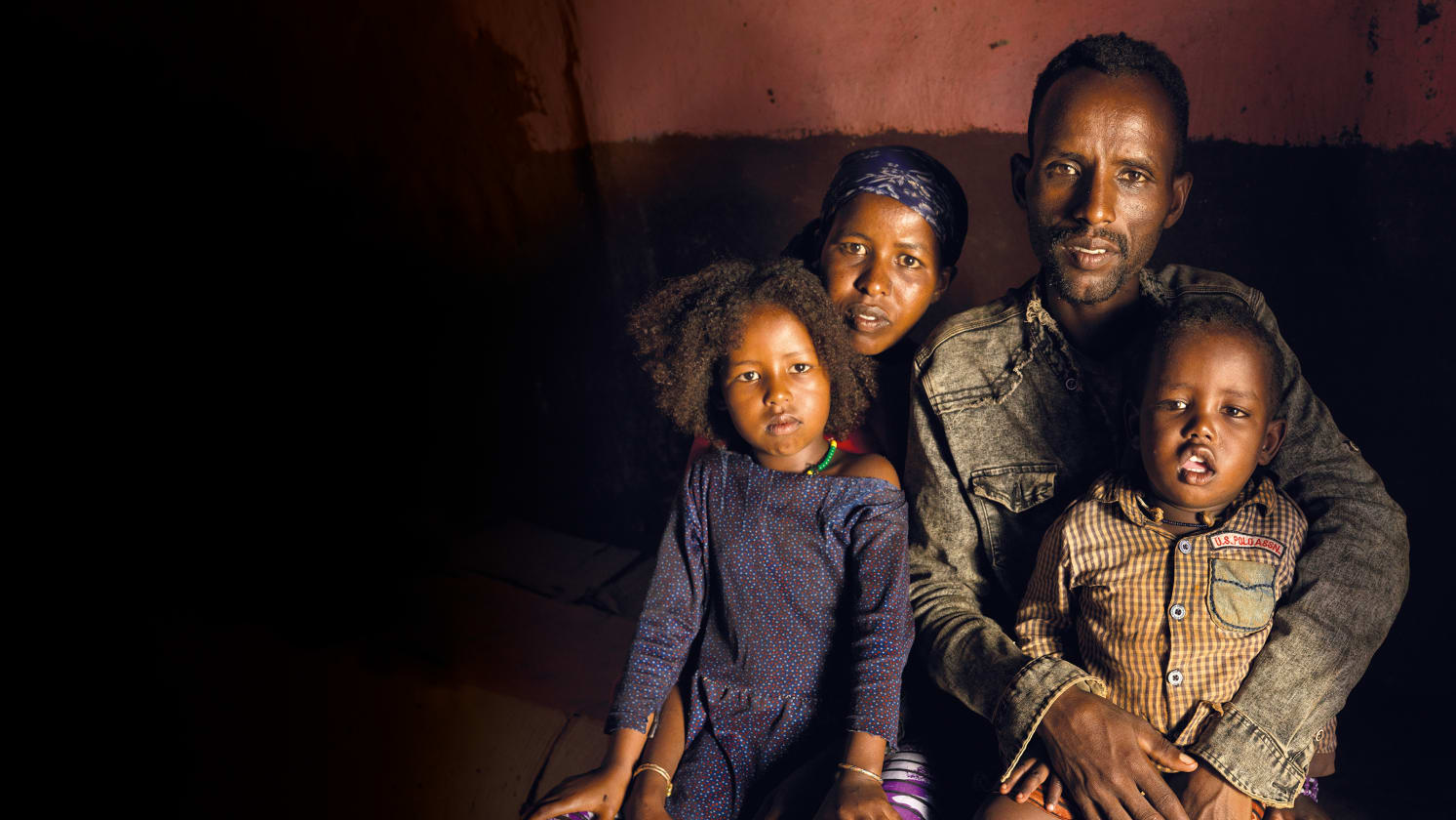 In a dark room a man and woman are sat, holding their children beside them.