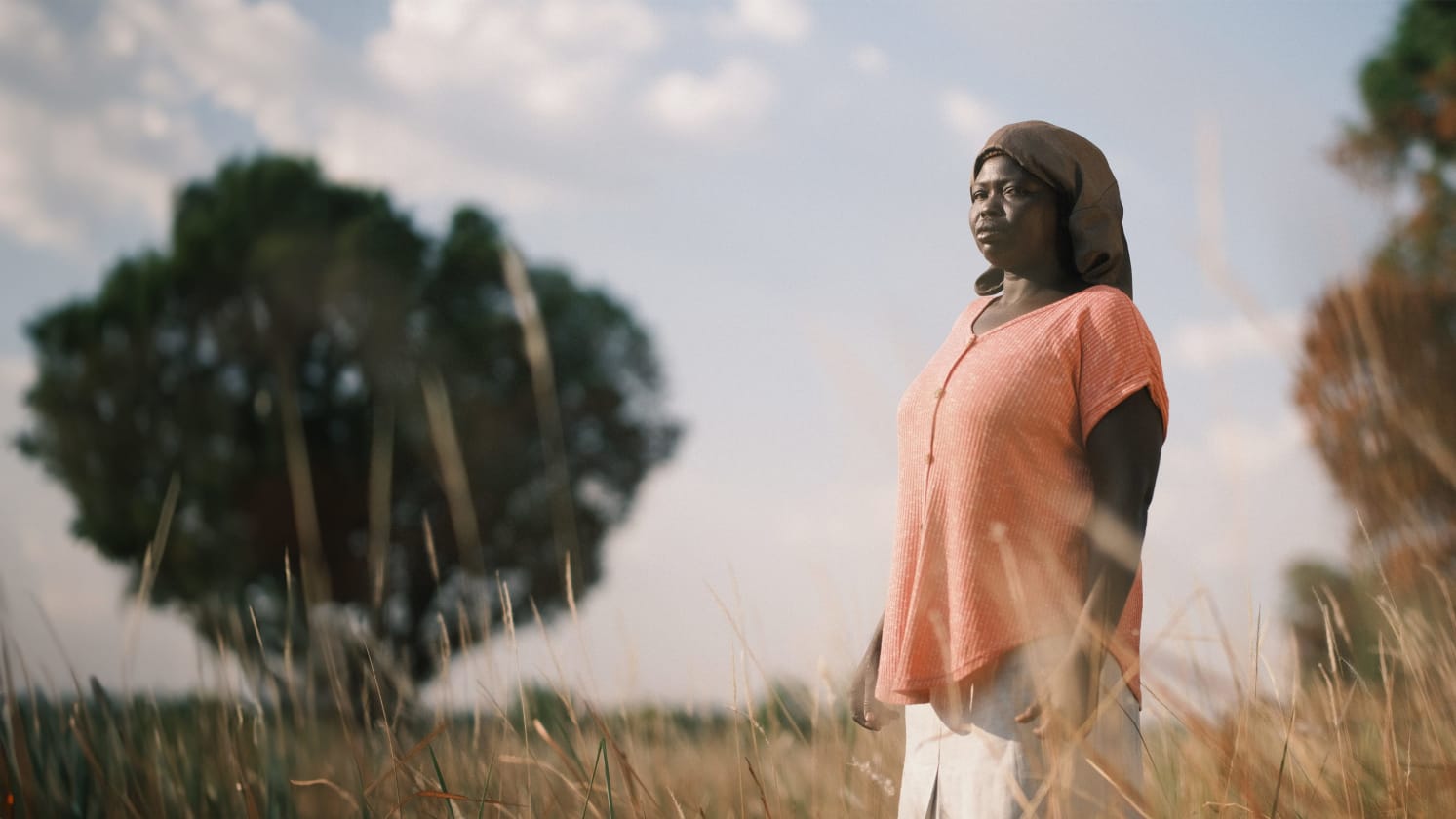 A woman is standing in a field, surrounded by grass and trees