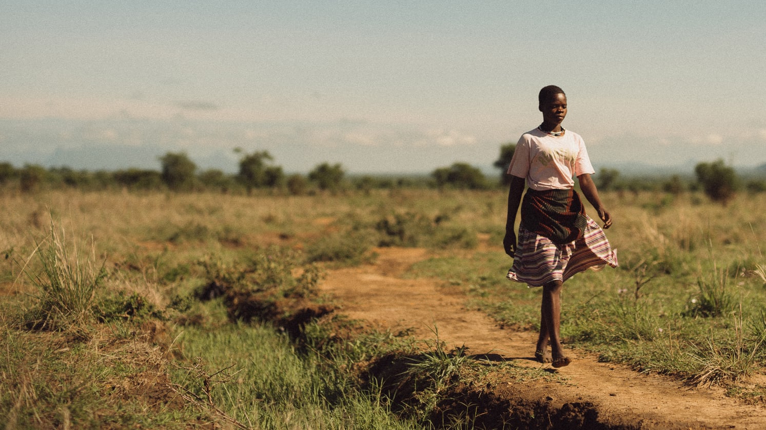 Esther, a young woman, walks along a path in a field.
