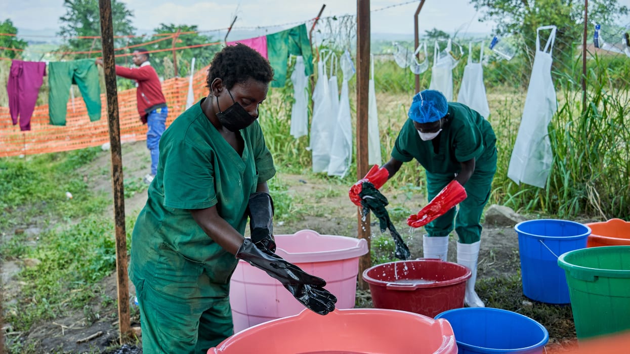 Two people wearing gloves and protective equipment wash in large bowls of water.