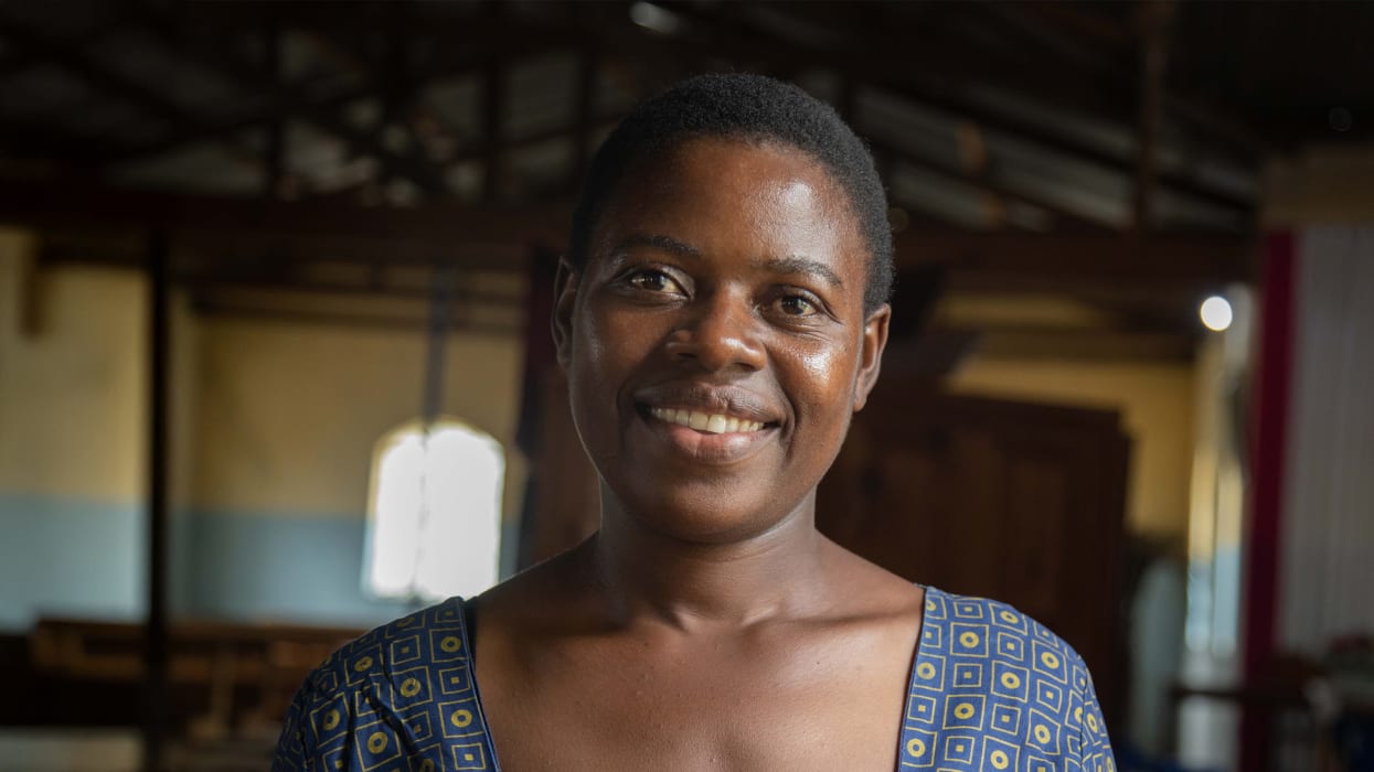 A woman stands in a dimly light building and smiles directly at the camera.