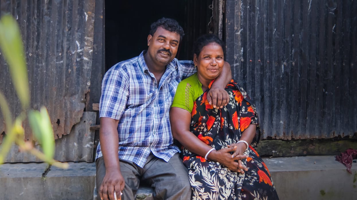 A smiling man and a woman sitting together in front of a corrugated metal building.